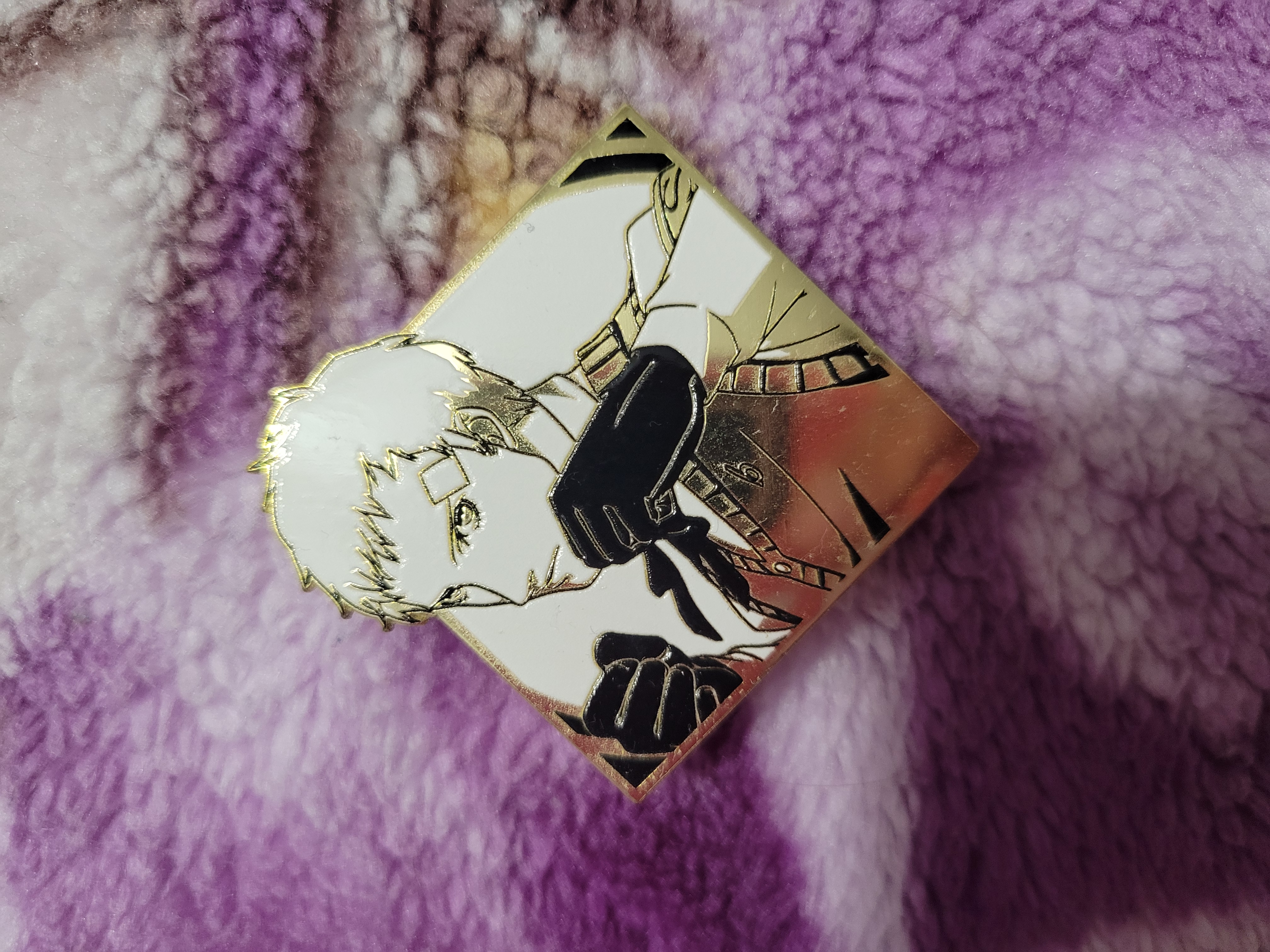 Akihiko Sanada with his fists out enamel pin on top of a colorful fuzzy blanket